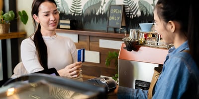 An image of a barista handing a payment terminal to customer holding their credit card.