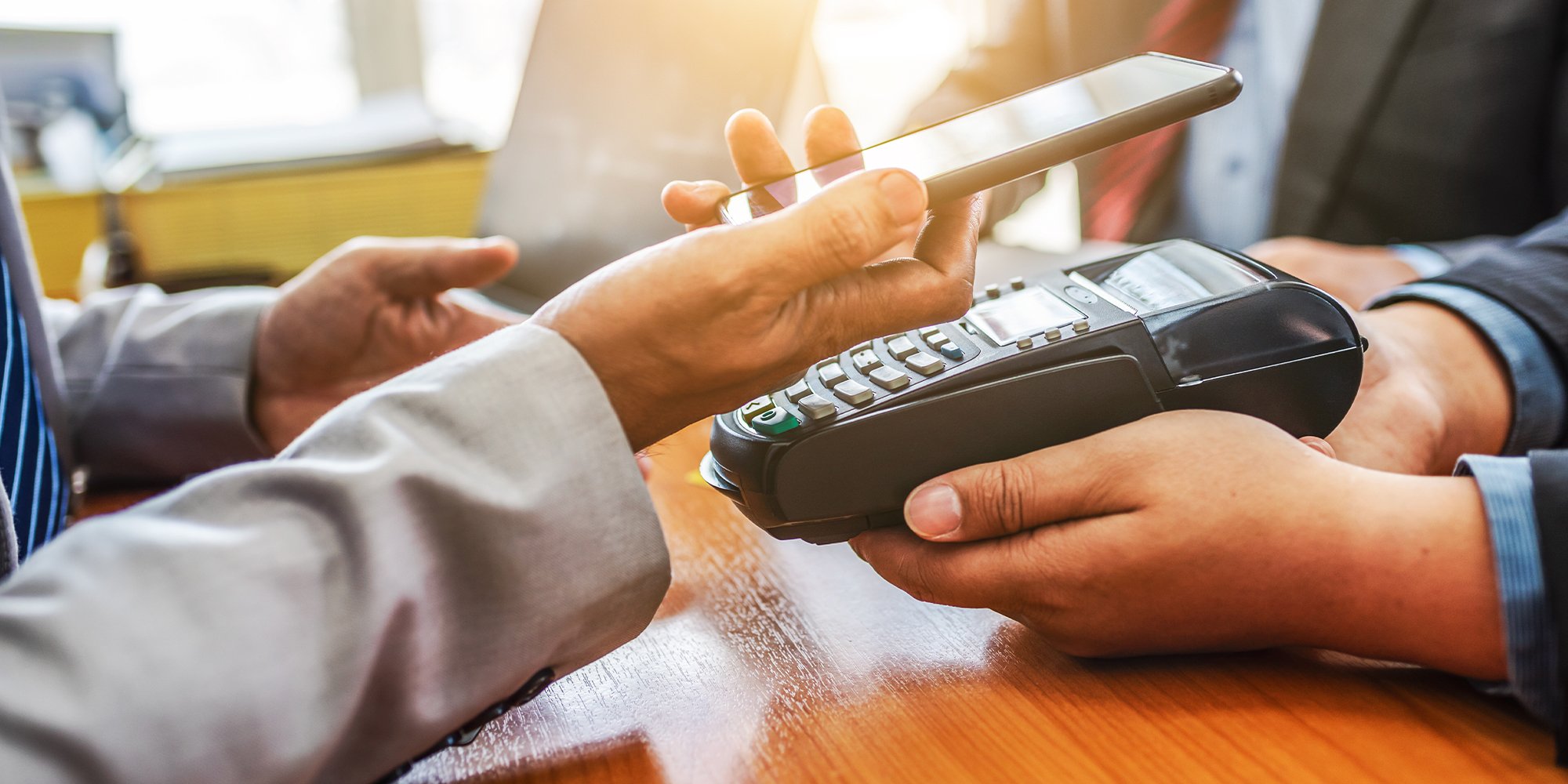 A trio of people setting a desk using a handheld payment terminal with a smartphone.