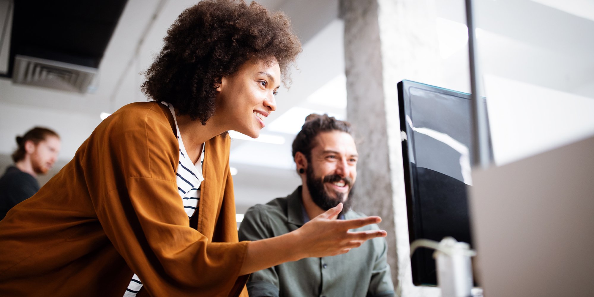 Two people smiling together while looking at a monitor in an office.